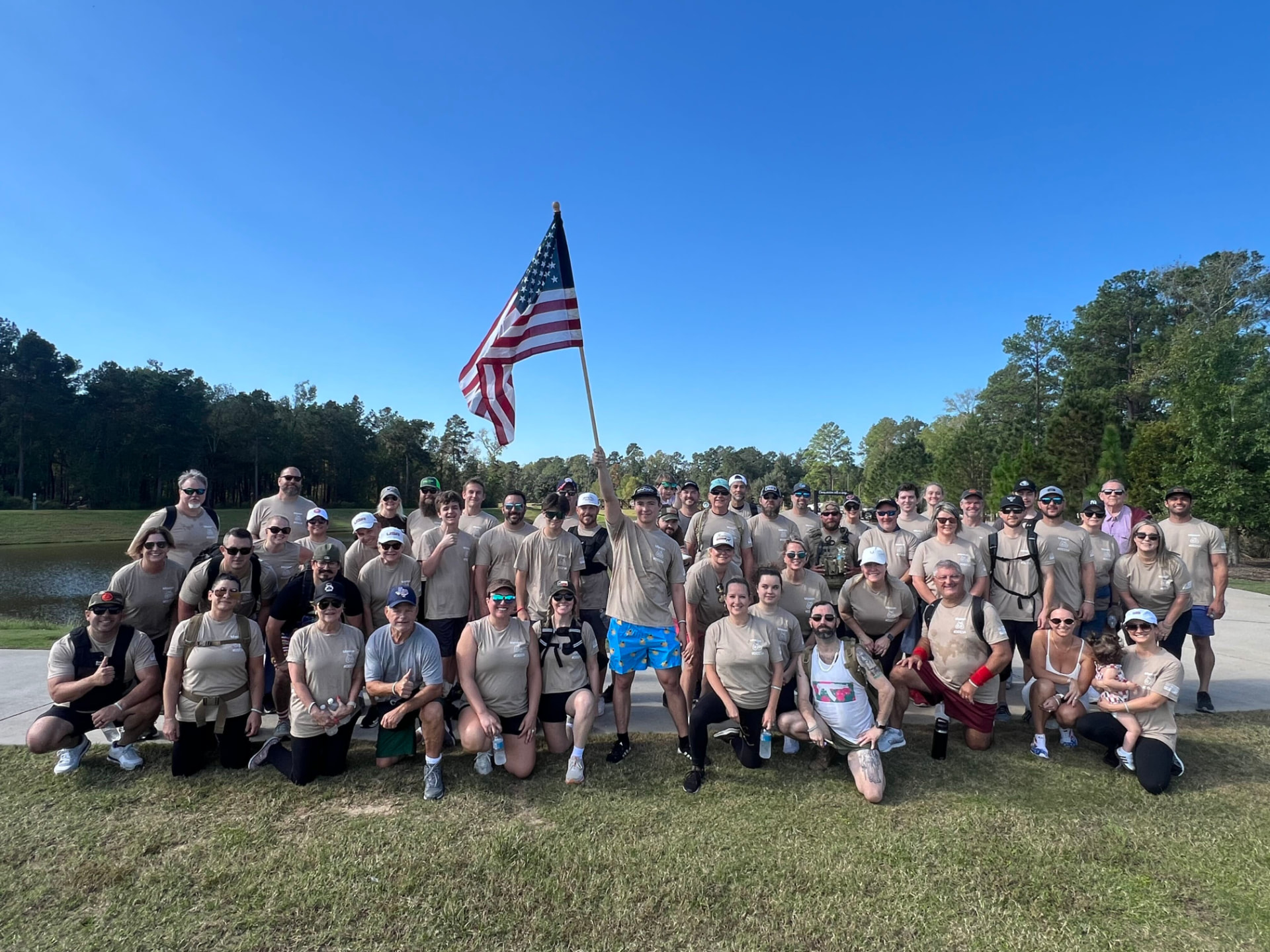 Large group photo of ruckers in tan event shirts raising the American flag by the pond