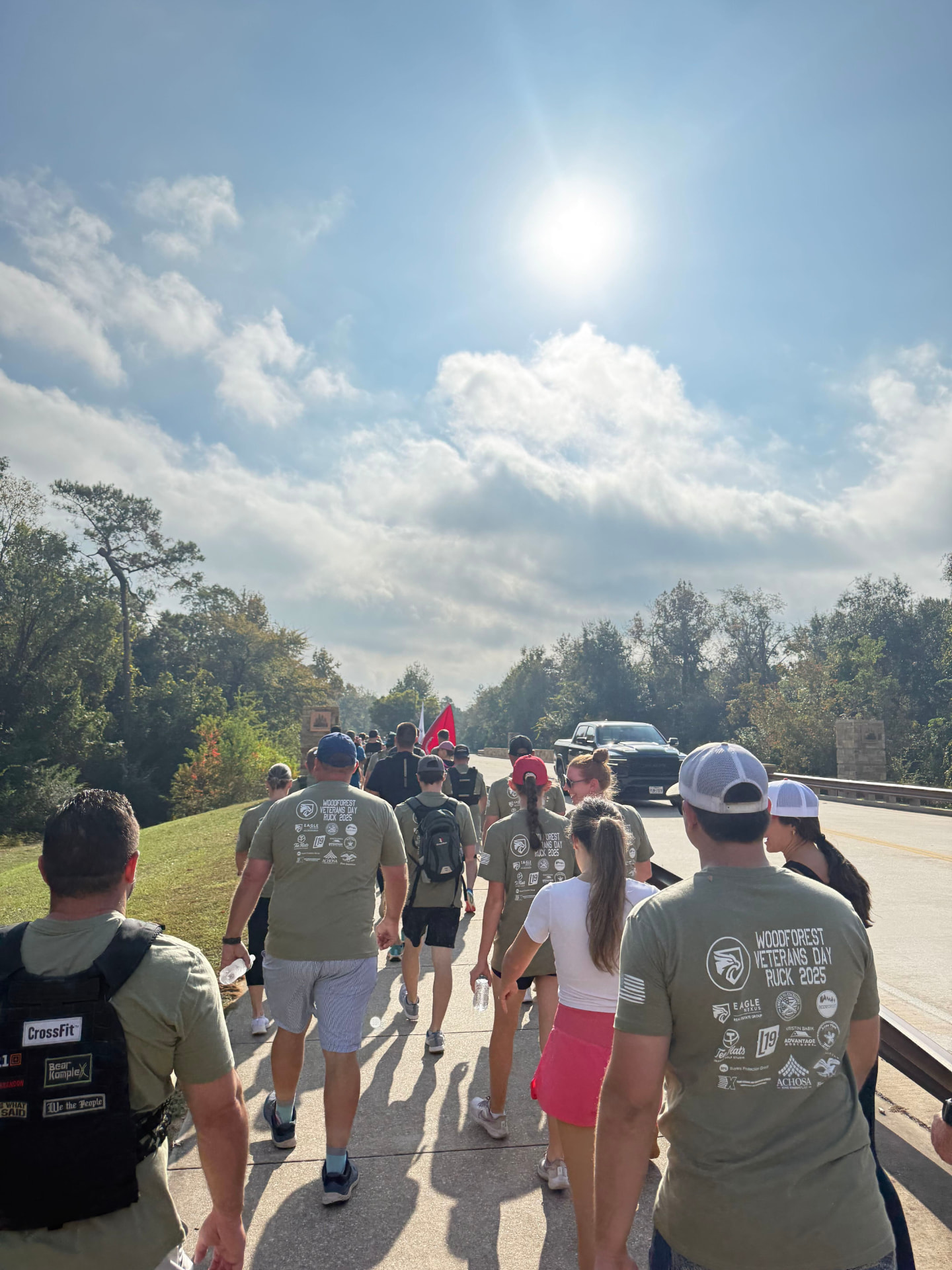 Ruckers in 2025 event shirts walking the sidewalk past the Woodforest entry monument