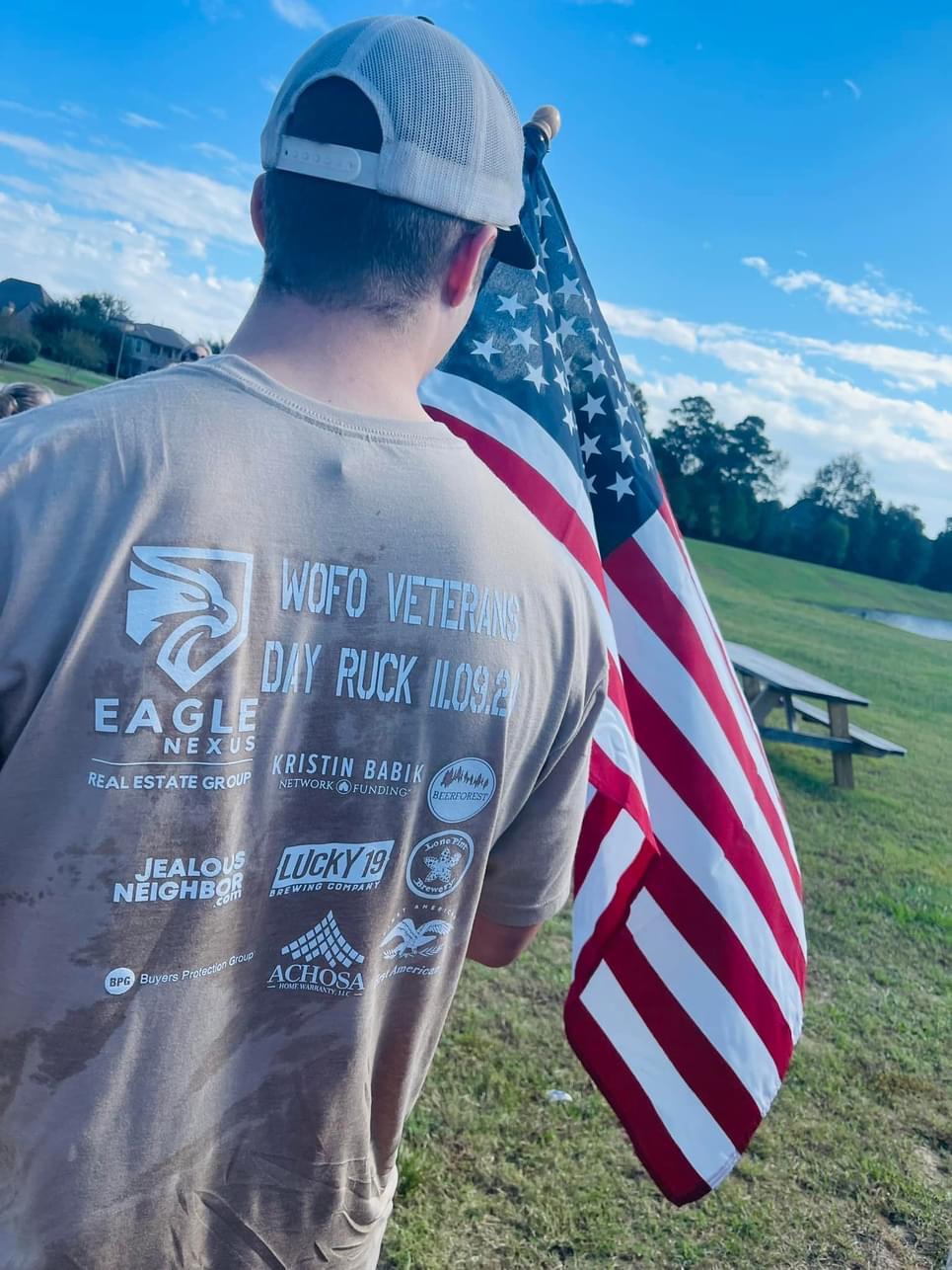 Rucker in an event shirt carrying the American flag across a Woodforest field