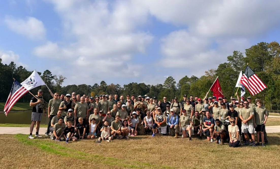 Group photo of the 2025 Woodforest Veterans Day Ruck with flags on the lawn