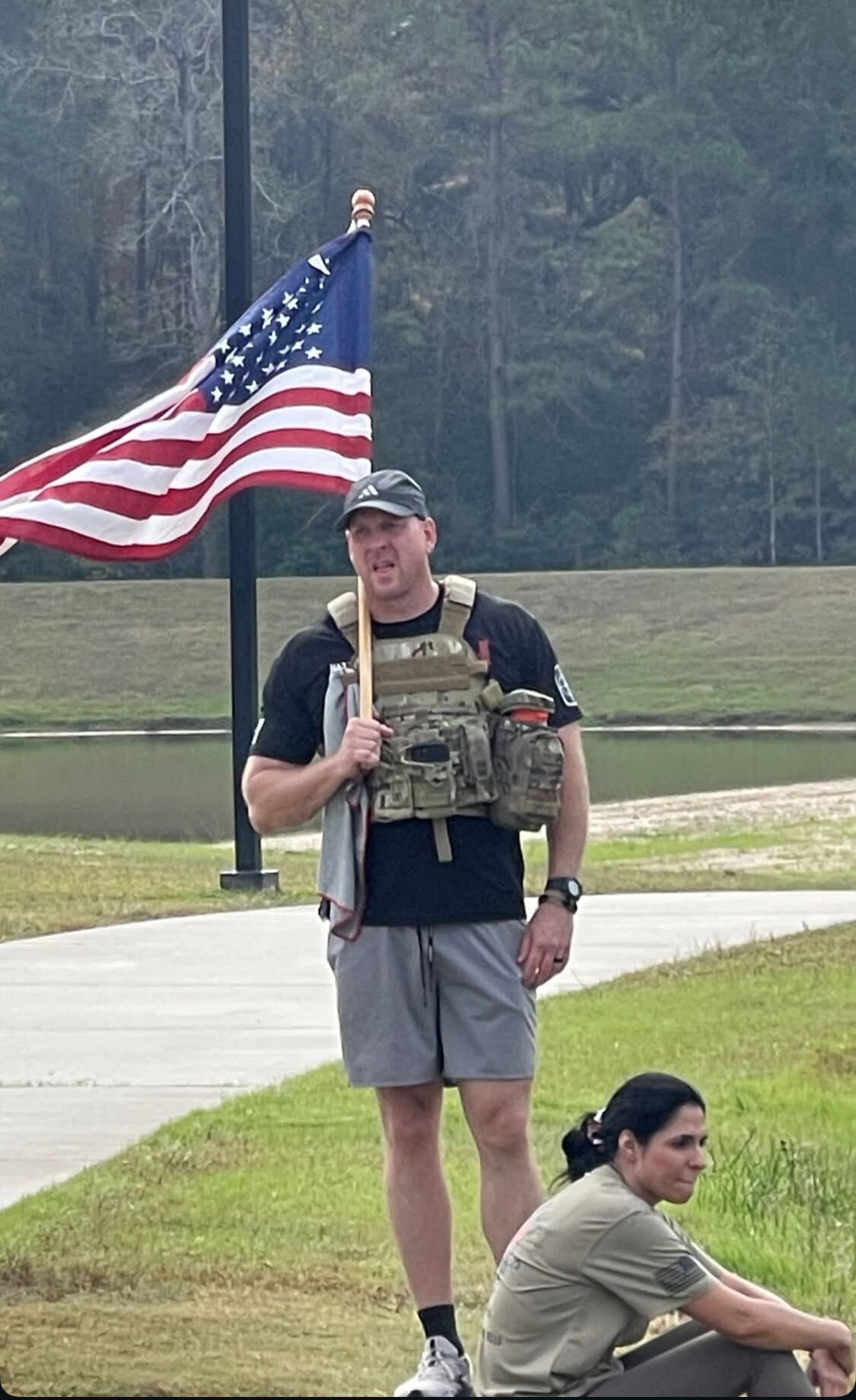 Veteran in a weighted plate carrier holding the American flag near the pond