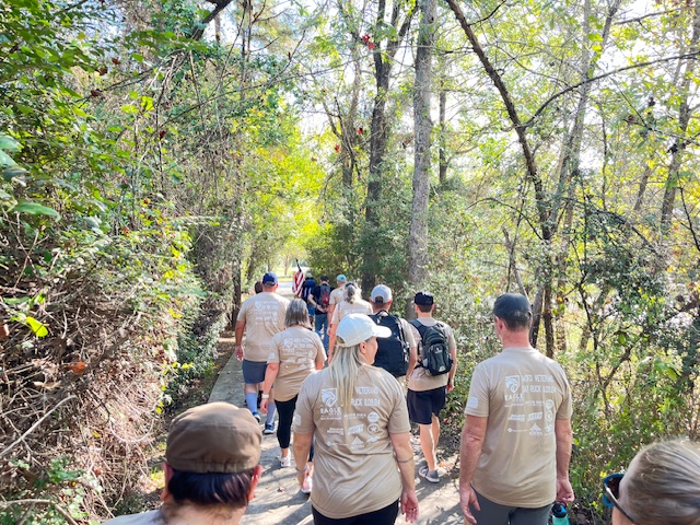 Group rucking a shaded wooded trail with the flag out front